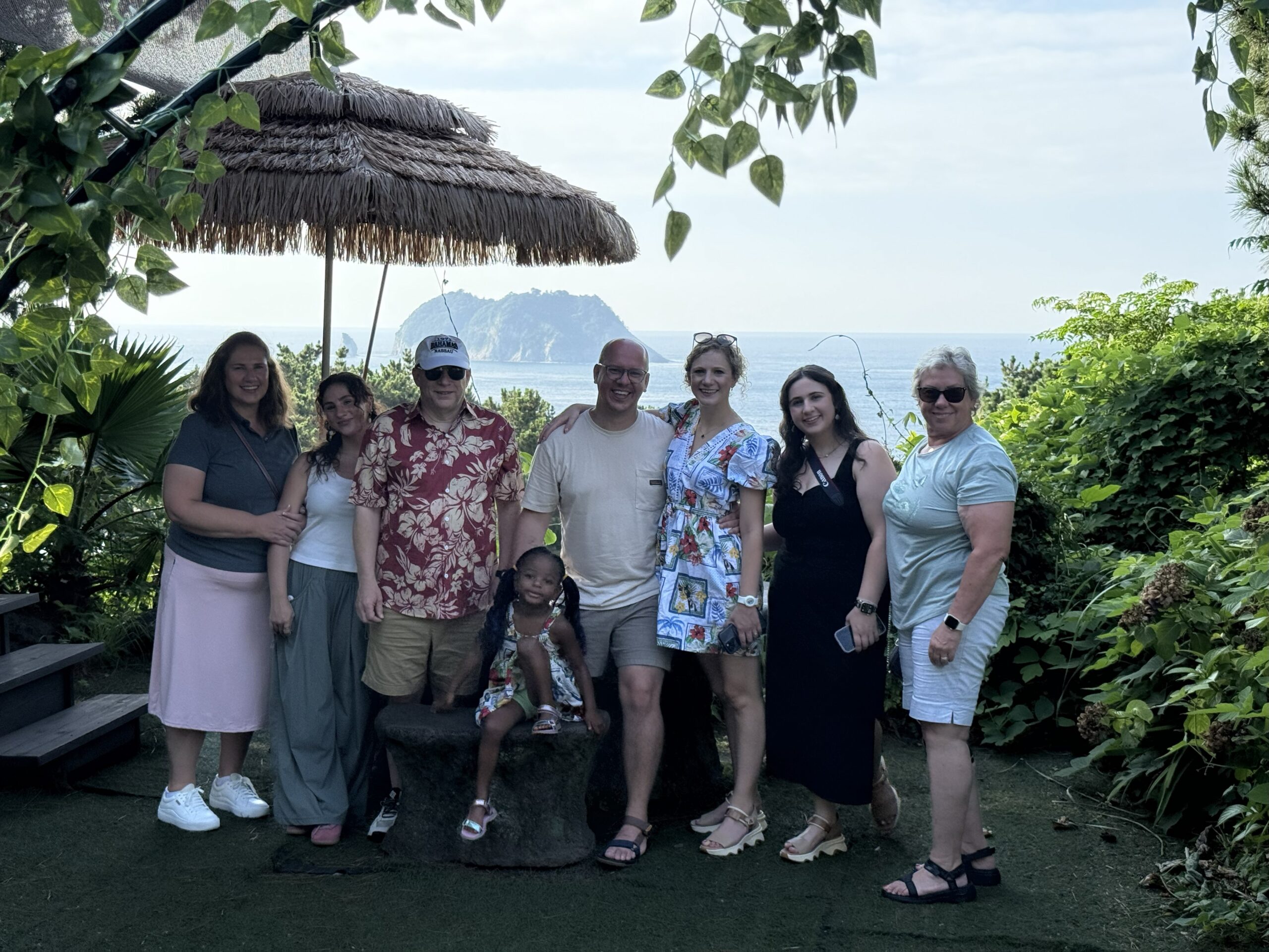 Family posing on a scenic cliffside with ocean and island views on Jeju Island, South Korea