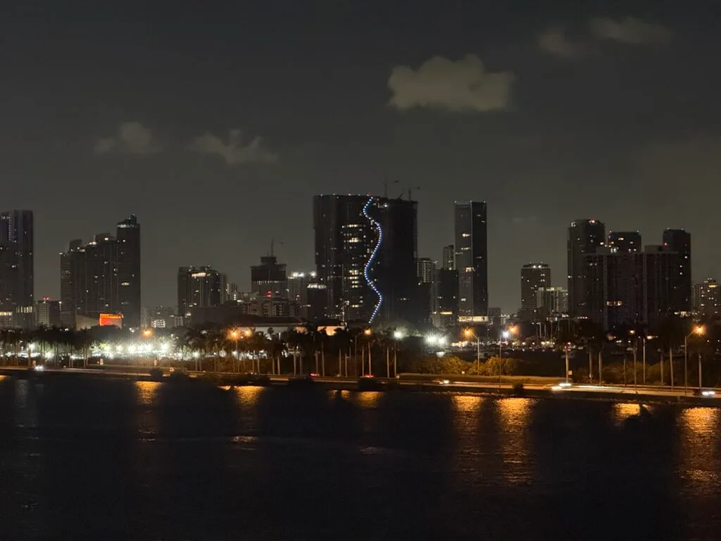 City skyline at night with illuminated high-rises viewed from a cruise ship returning to port.