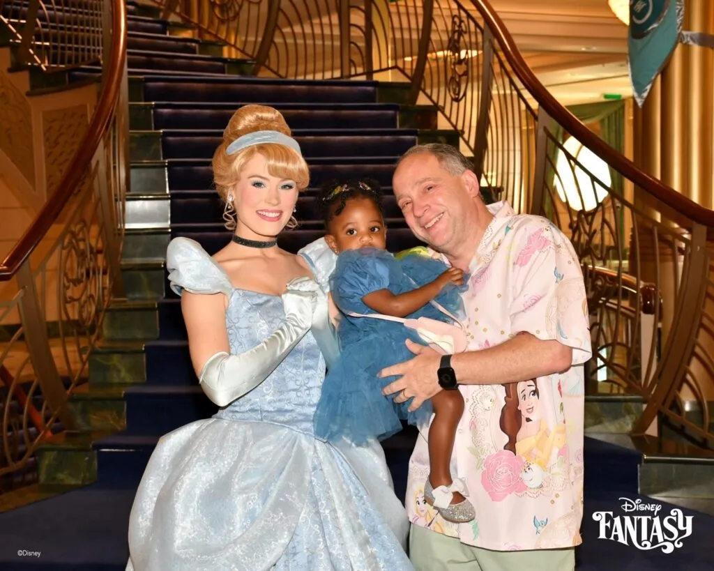 Child wearing a princess dress and family wearing Disney themed shirts meeting Cinderella on a Disney cruise
