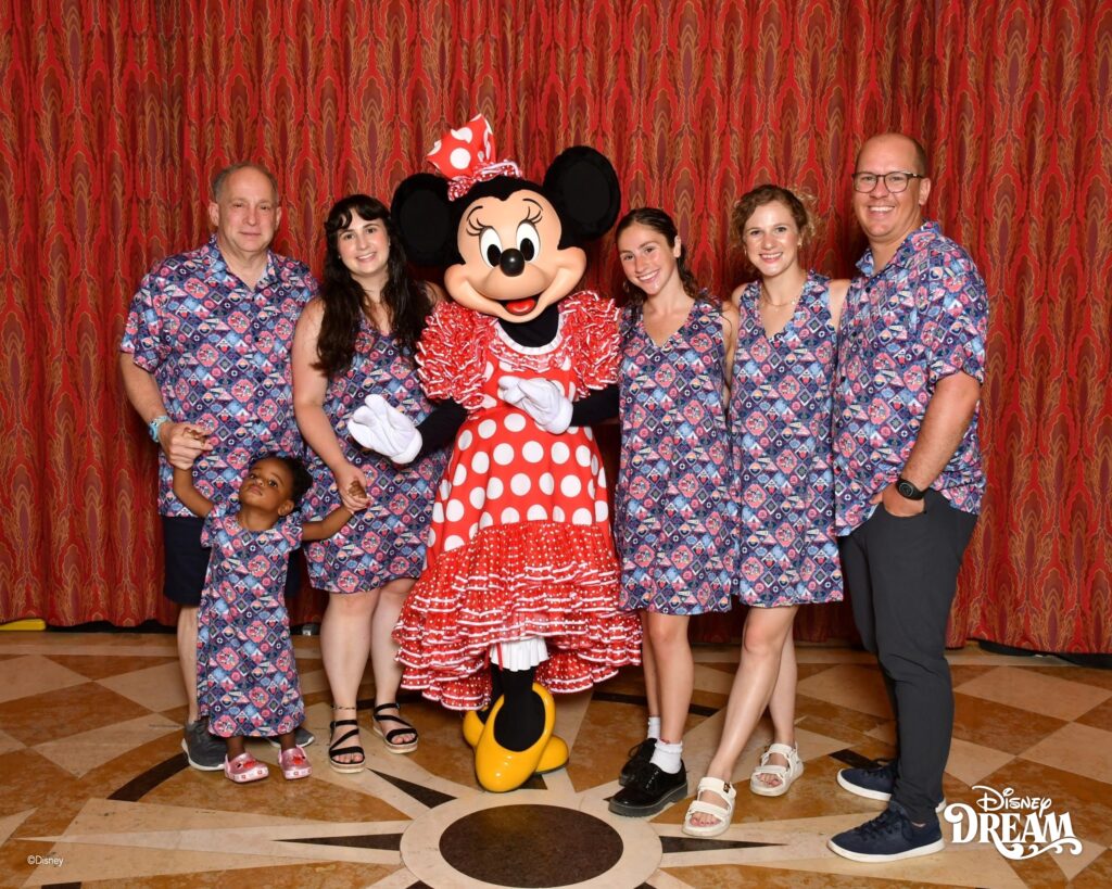 Family wearing matching family vacation outfits, Disney themed shirts posing with Minnie Mouse on a Disney cruise