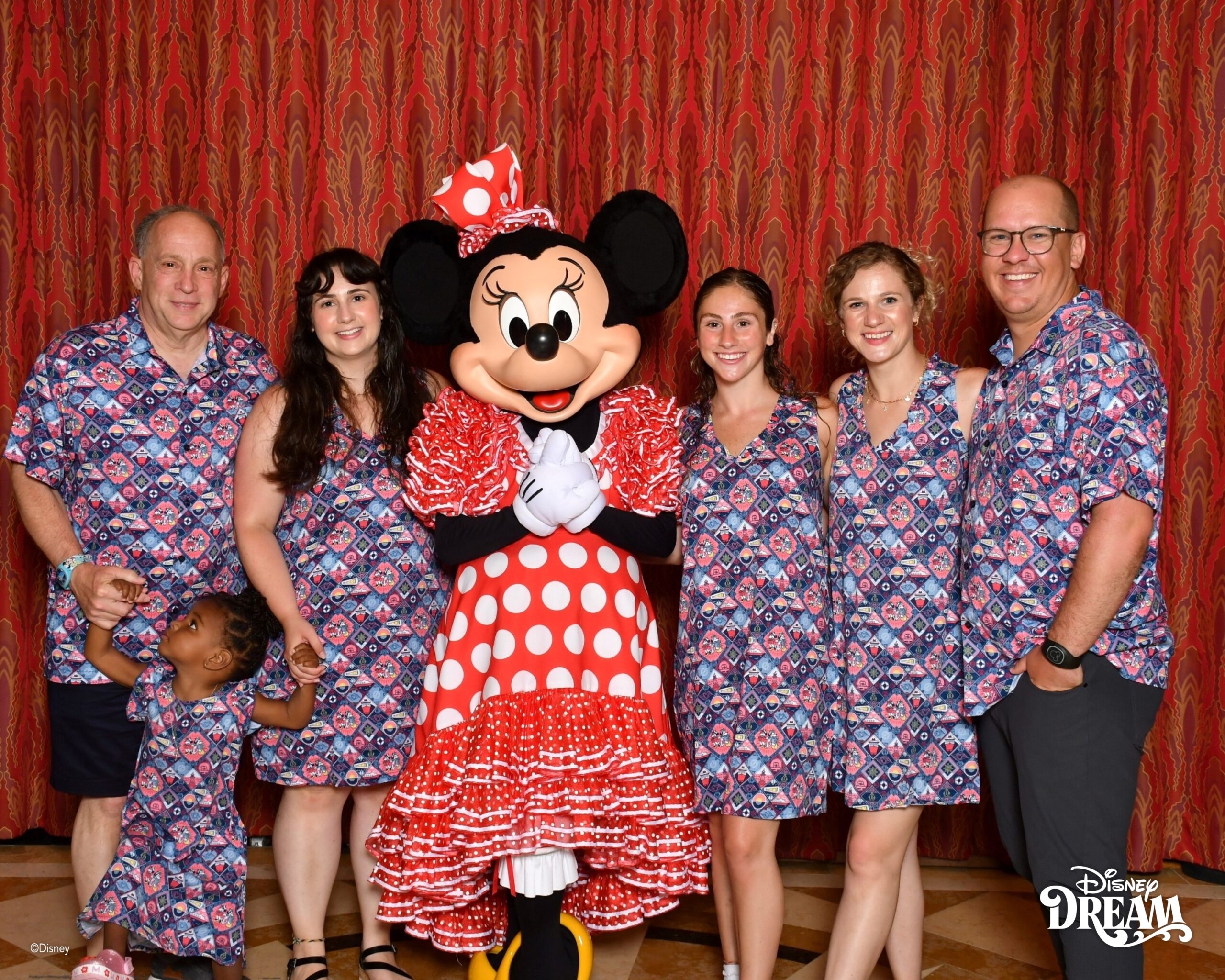 Family wearing matching Disney themed shirts posing with Minnie Mouse on a Disney cruise