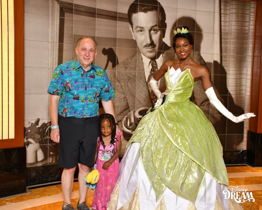 Child wearing a princess dress posing with Princess Tiana on Disney Cruise Line